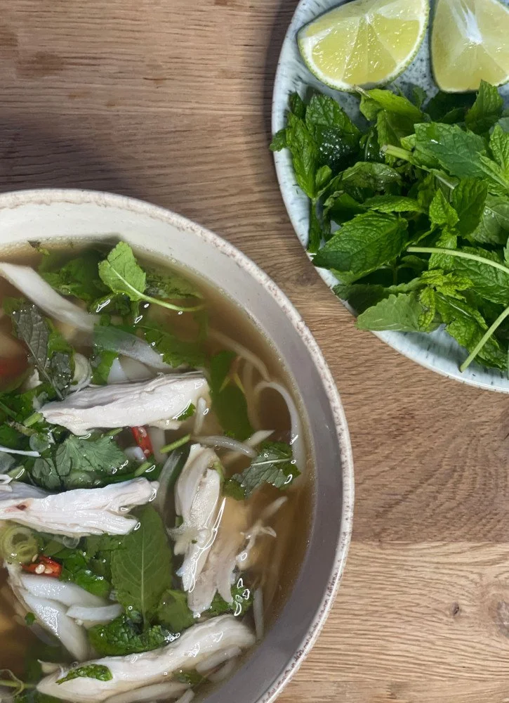 Photo of bowl of chicken pho and plate of mint leaves with cut limes