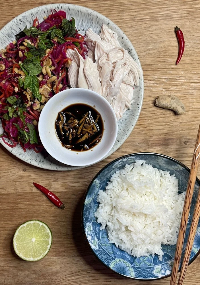 Photo of plate of poached chicken with goi and a bowl of rice.